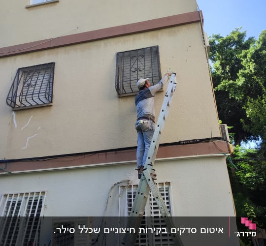 אדם על סולם אוטם קיר חיצוני של בניין